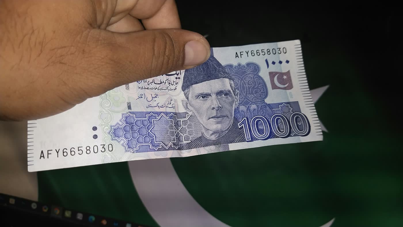 A hand holding a Pakistani one thousand rupee note